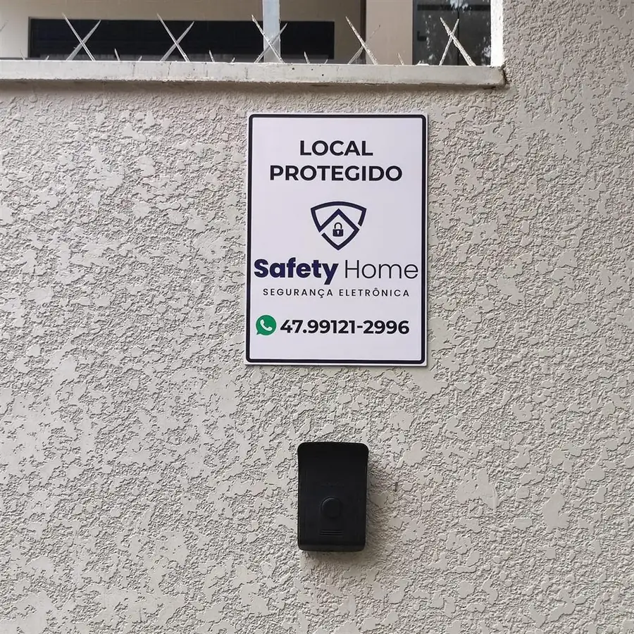 Placa Local Protegido da Safety Home acima de leitor de acesso no muro