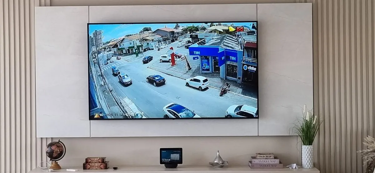 Sala com painel ripado e TV mostrando a imagem das câmeras da rua