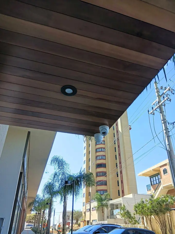 Duas câmeras tipo domo instaladas no forro de madeira da entrada de um prédio, com uma rua e um edifício ao fundo